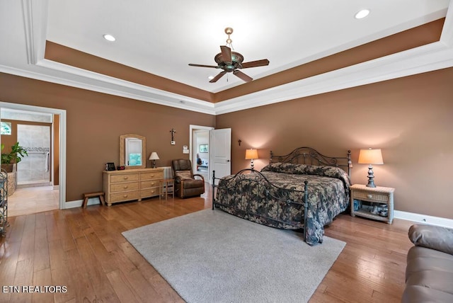 bedroom with light wood-type flooring, ceiling fan, and a raised ceiling