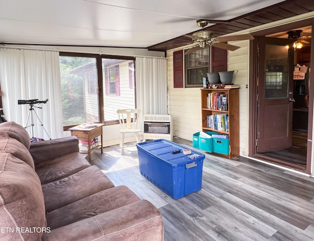 living room featuring ceiling fan, wood walls, heating unit, and hardwood / wood-style floors