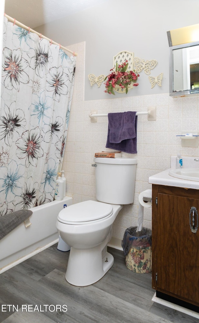 full bathroom featuring toilet, vanity, tile walls, hardwood / wood-style floors, and shower / bath combo with shower curtain