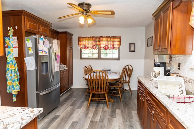 kitchen with ceiling fan, stainless steel refrigerator with ice dispenser, hardwood / wood-style flooring, light stone countertops, and a textured ceiling