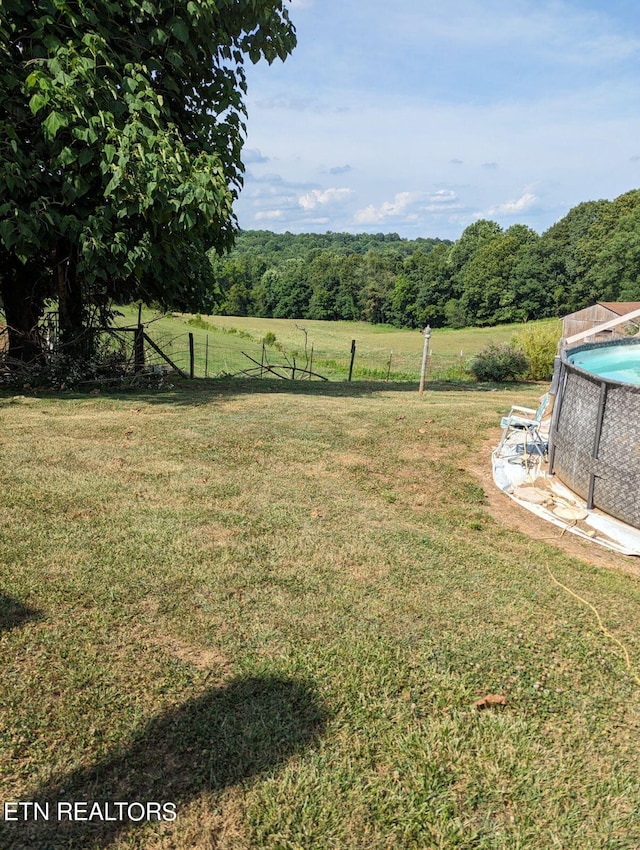 view of yard with a rural view, fence, a fenced in pool, and a view of trees