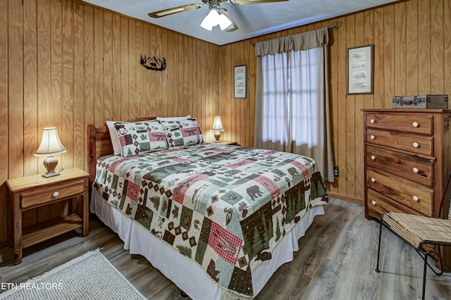 bedroom featuring ceiling fan, wooden walls, and hardwood / wood-style flooring