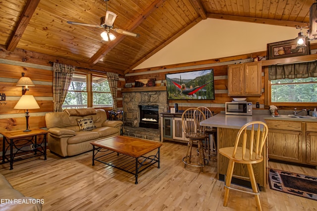 living room with wooden ceiling, beamed ceiling, a stone fireplace, and light hardwood / wood-style flooring