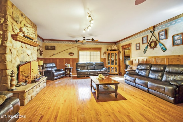 living room with track lighting, hardwood / wood-style floors, a stone fireplace, ceiling fan, and ornamental molding