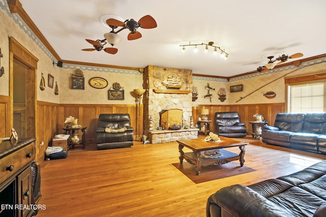 living room featuring a stone fireplace, track lighting, ornamental molding, and ceiling fan