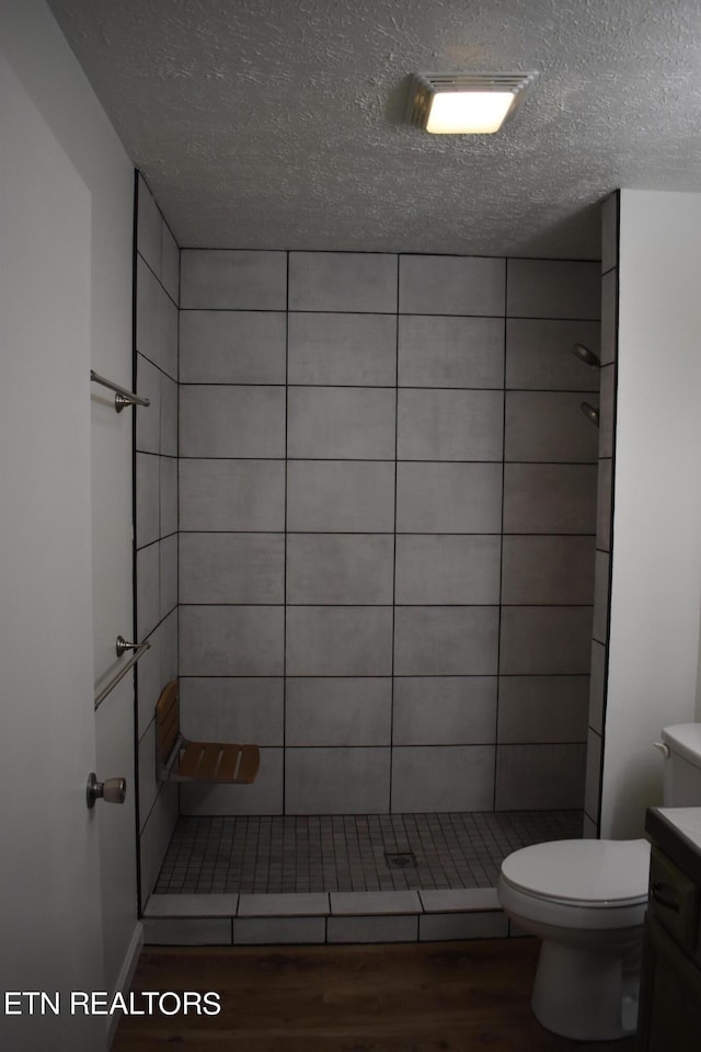 bathroom with toilet, vanity, hardwood / wood-style floors, and a tile shower