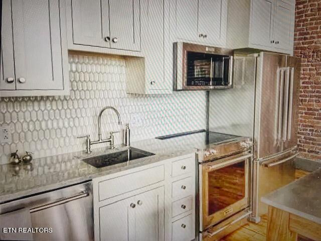 kitchen featuring decorative backsplash, light stone counters, sink, and appliances with stainless steel finishes