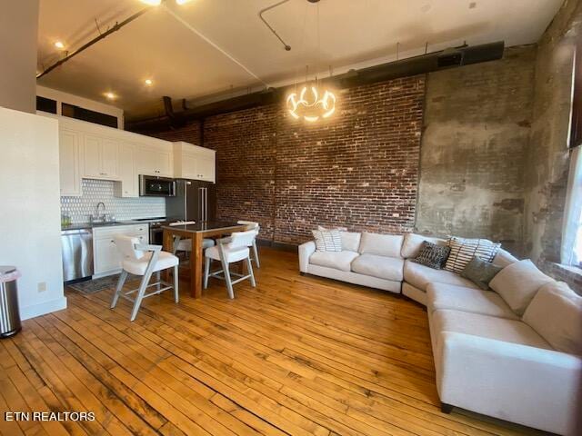 living room featuring sink, a towering ceiling, light hardwood / wood-style flooring, and brick wall