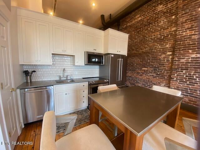 kitchen featuring brick wall, appliances with stainless steel finishes, white cabinets, and sink