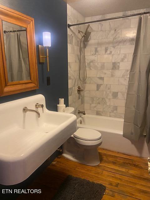 bathroom with wood-type flooring, toilet, and shower / bath combo with shower curtain