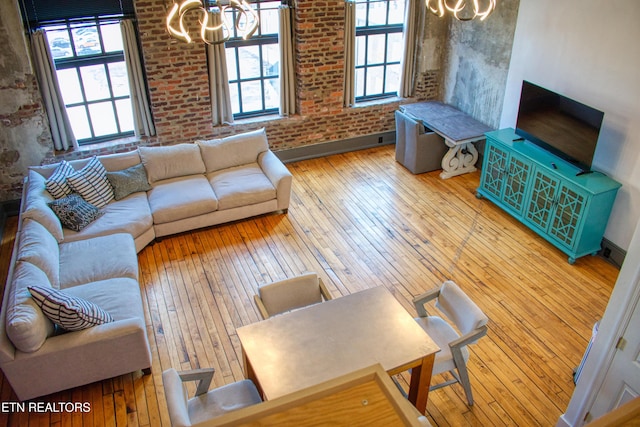 living room with light hardwood / wood-style floors, brick wall, and an inviting chandelier