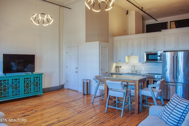 kitchen with stainless steel appliances, a towering ceiling, light hardwood / wood-style floors, decorative backsplash, and white cabinets