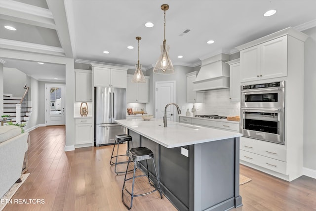 kitchen featuring sink, white cabinets, light wood-type flooring, custom exhaust hood, and appliances with stainless steel finishes