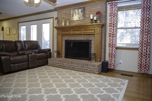 living room featuring crown molding, ceiling fan, hardwood / wood-style floors, a textured ceiling, and a brick fireplace