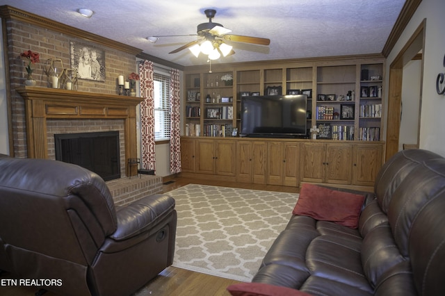 living room with wood-type flooring, a textured ceiling, ornamental molding, ceiling fan, and a fireplace