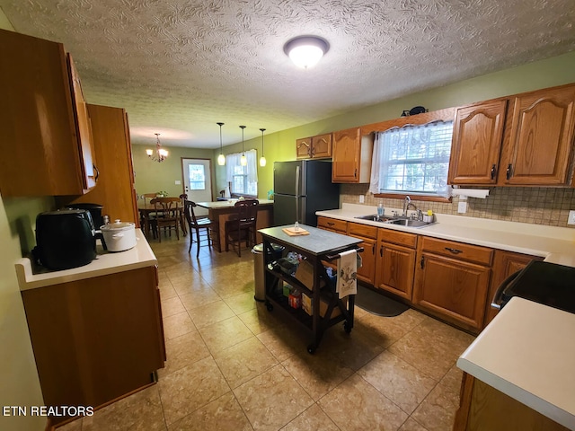 kitchen with sink, stainless steel fridge, a chandelier, pendant lighting, and decorative backsplash