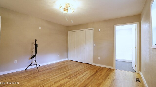 unfurnished bedroom featuring wood-type flooring, a closet, and ensuite bath