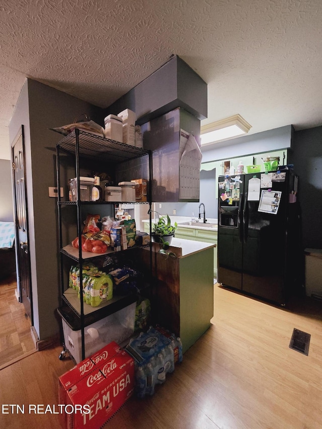 kitchen featuring a textured ceiling, light hardwood / wood-style floors, black fridge, kitchen peninsula, and green cabinetry