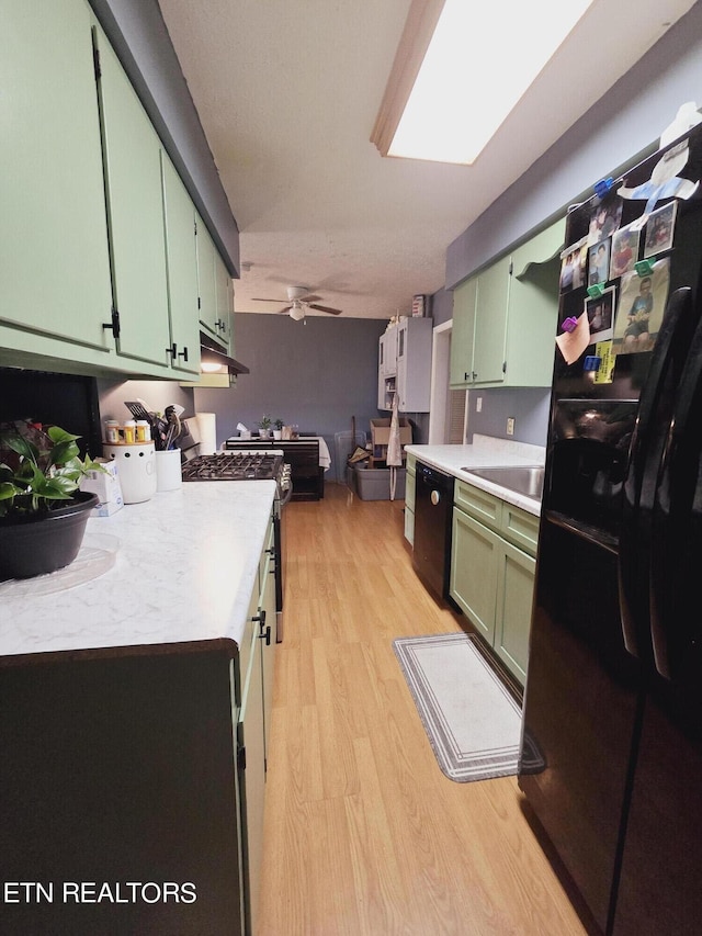 kitchen with ceiling fan, sink, green cabinetry, light hardwood / wood-style flooring, and black appliances