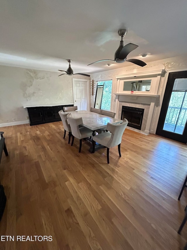 unfurnished dining area with hardwood / wood-style flooring, ceiling fan, and a tiled fireplace