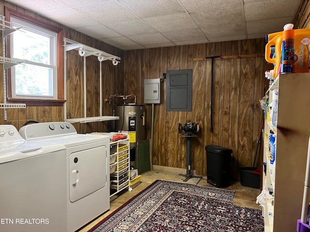 laundry area featuring electric panel, water heater, wooden walls, and separate washer and dryer