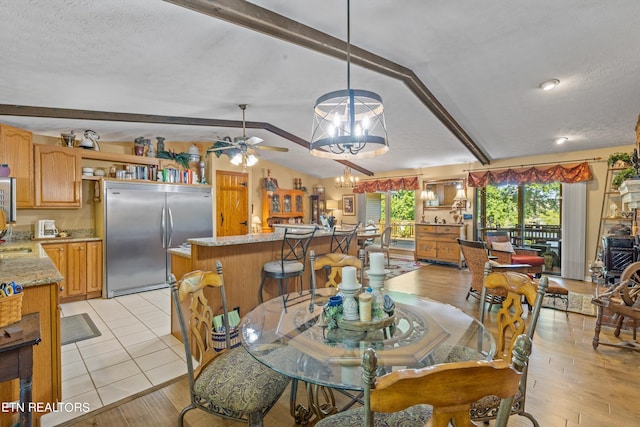 dining area with ceiling fan with notable chandelier, a textured ceiling, lofted ceiling with beams, and light hardwood / wood-style floors