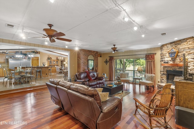 living room featuring ceiling fan, a stone fireplace, and hardwood / wood-style floors