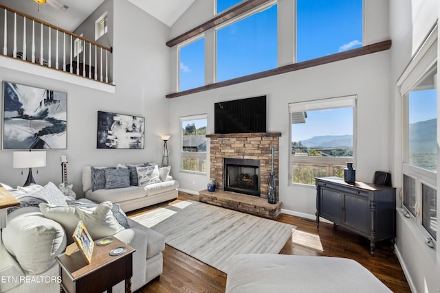 living room featuring ceiling fan, dark hardwood / wood-style floors, a towering ceiling, and a fireplace