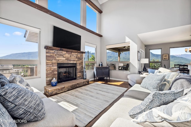 living room with an inviting chandelier, a stone fireplace, a towering ceiling, and hardwood / wood-style flooring