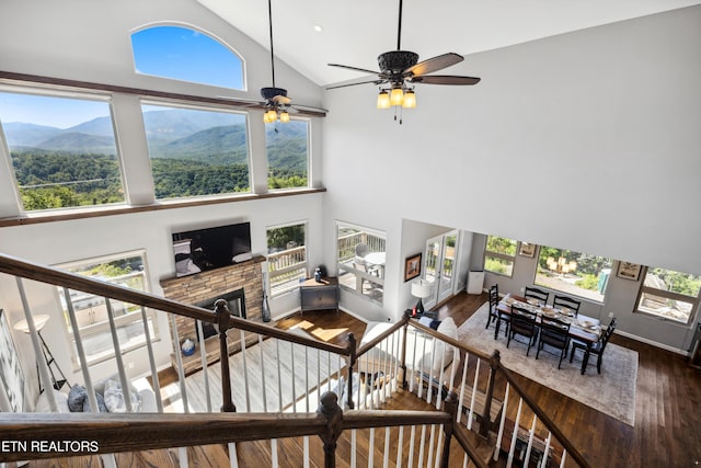 staircase featuring ceiling fan, hardwood / wood-style floors, high vaulted ceiling, and a stone fireplace