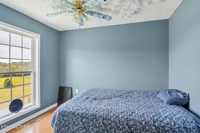 bedroom with multiple windows, ceiling fan, and hardwood / wood-style floors