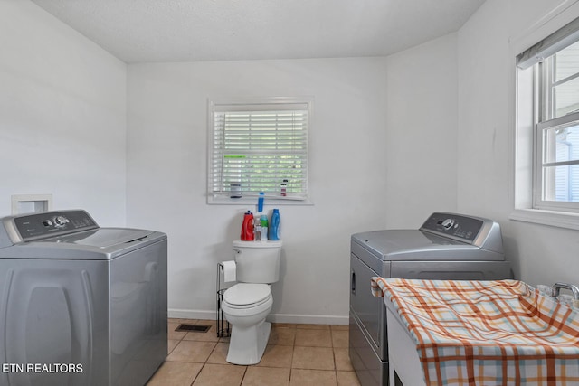 laundry area featuring light tile patterned flooring, washing machine and clothes dryer, and a healthy amount of sunlight