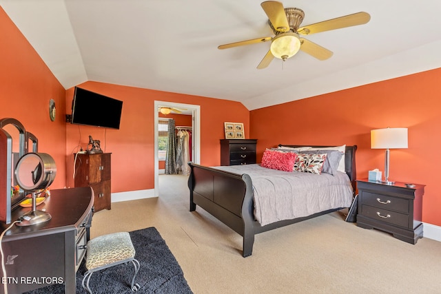 carpeted bedroom with vaulted ceiling, a walk in closet, and ceiling fan