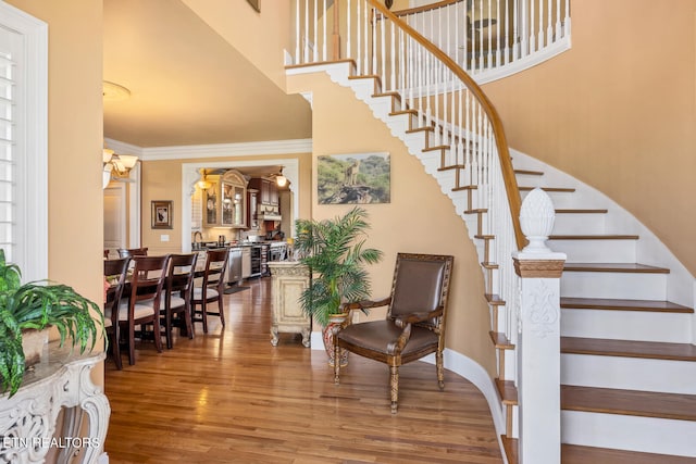 stairway featuring wood-type flooring, crown molding, and a high ceiling