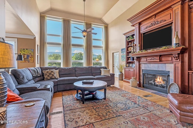 living room featuring ceiling fan, a fireplace, light hardwood / wood-style flooring, and high vaulted ceiling