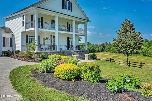 view of front facade with a balcony, a porch, and a front lawn