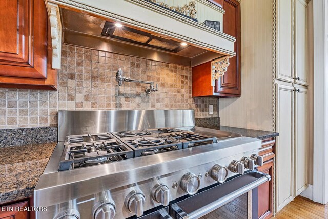 interior space featuring dark stone countertops, light wood-type flooring, range with gas cooktop, and tasteful backsplash