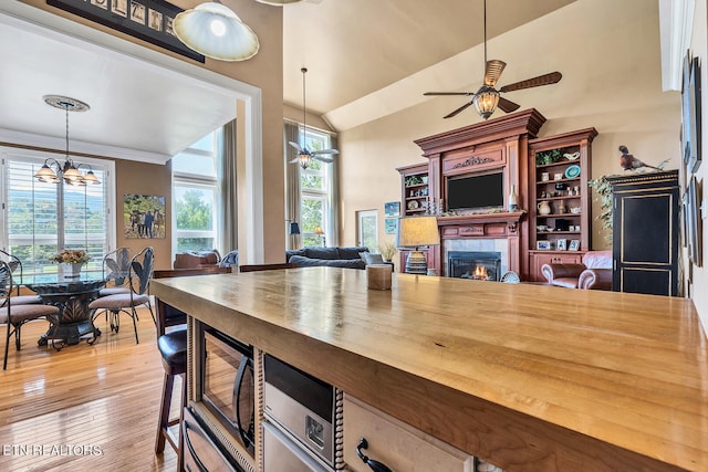 kitchen with wooden counters, light hardwood / wood-style flooring, ceiling fan with notable chandelier, and a tiled fireplace