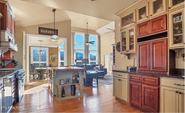 kitchen with range with two ovens, hanging light fixtures, ceiling fan with notable chandelier, high vaulted ceiling, and light hardwood / wood-style floors