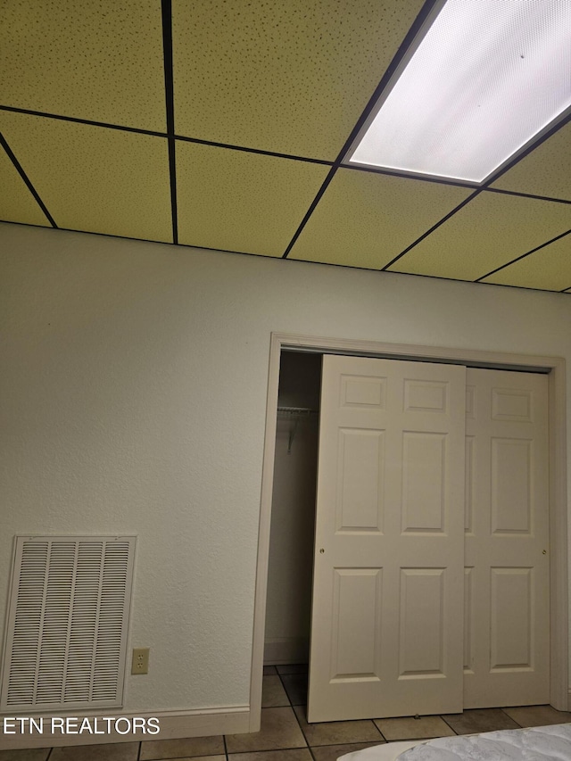 unfurnished bedroom featuring a drop ceiling, light tile patterned floors, and a closet