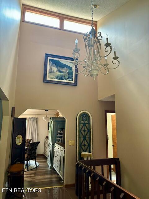 interior space featuring a towering ceiling, a notable chandelier, a textured ceiling, and dark wood-type flooring