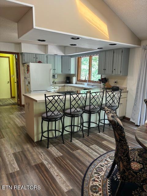 kitchen featuring vaulted ceiling, a peninsula, a breakfast bar area, and freestanding refrigerator