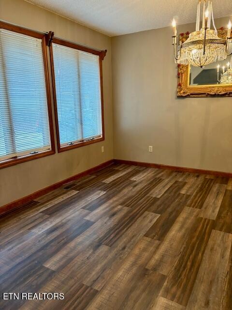 unfurnished dining area with dark wood-type flooring, an inviting chandelier, and a textured ceiling