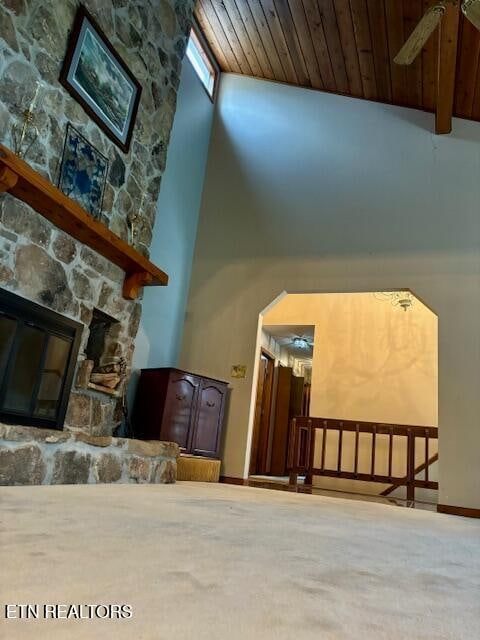 interior space featuring wooden ceiling, baseboards, a stone fireplace, and a towering ceiling