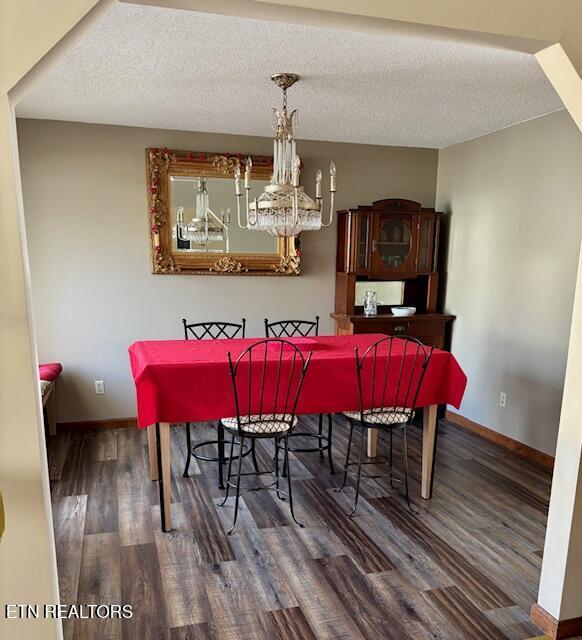 dining area featuring baseboards, a textured ceiling, an inviting chandelier, and wood finished floors