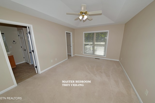 carpeted empty room with ceiling fan and a tray ceiling