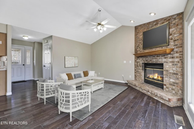 living room featuring dark wood-type flooring, ceiling fan, vaulted ceiling, and a brick fireplace