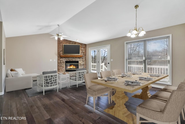 dining area featuring dark wood-type flooring, lofted ceiling, ceiling fan with notable chandelier, and a brick fireplace