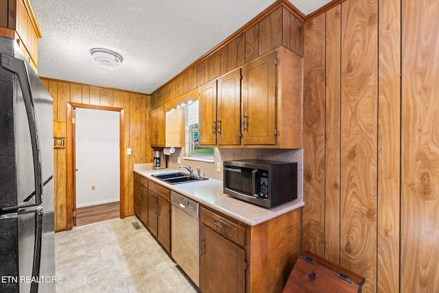 kitchen featuring sink, wooden walls, stainless steel appliances, ornamental molding, and a textured ceiling