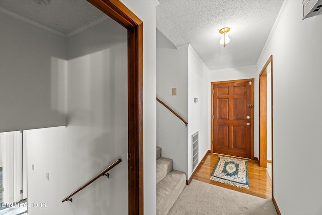 entryway featuring light colored carpet, ornamental molding, and a textured ceiling